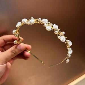 Detailed close-up of a gold hairband with white resin roses and pearls held in hand