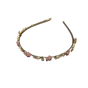 Serre-tête floral doré avec pétales roses et perles sur un fond blanc épuré