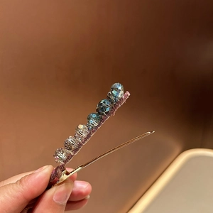 Detail view of gold crystal hair clip with gradient blue beads and purple ribbon