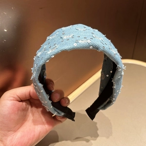 Macro detail of light blue denim headband with silver sequins and distressed edge texture