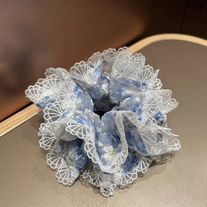 Détail d'un chouchou bleu fleuri en seersucker avec bordure en dentelle blanche et pompons