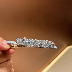 Detail view of crystal beads on a gold duckbill hair clip with gray fabric wrapping