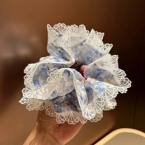 Détail d'un chouchou bleu fleuri en seersucker avec bordure en dentelle blanche et franges