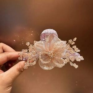 Dettaglio di un fermaglio per capelli con fiore in organza champagne e perline di cristallo