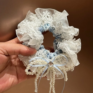Détail d'un chouchou floral avec nœud en dentelle, cristal et glands en perles