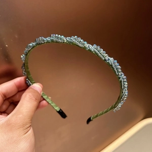 Detail eines handgefertigten Haarreifs aus grünem Samt mit hellblauen Kristallperlen