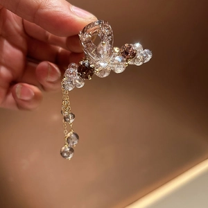Elegant gold hair claw with shimmering crystals and tassel pendants shown on a warm background