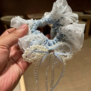 Détail d'un chouchou bleu floral avec dentelle, nœud en perles et pampilles en cristal