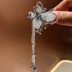 Detail of silver butterfly hair claw with blue and white beaded tassels on warm backdrop