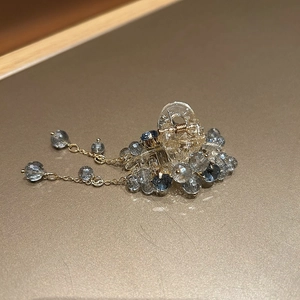 Detail of mini hair claw clip featuring blue crystals and elegant metallic tassels