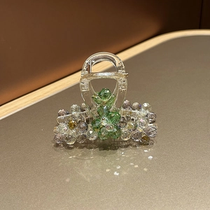 Detailed close-up of crystal beads woven into floral patterns on a clear resin hair claw