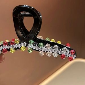 Detail of shark hair claw clip with colorful crystal beads on black acrylic surface