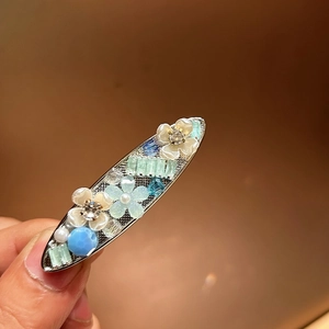 Close-up of alloy hair clip with mother-of-pearl flowers, crystals, and pearls