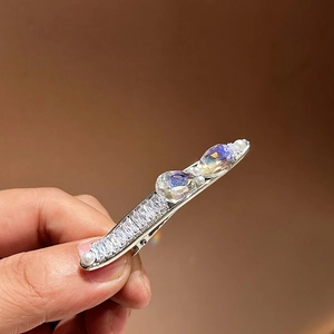 Pince à cheveux argentée avec strass verts et perles tenue à la main sur fond brun