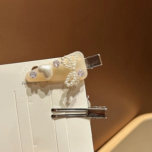 Détail d'une pince à cheveux crème avec nœud en perles, motif cœur et cristaux brillants