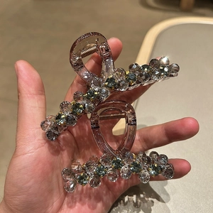 Detailed view of grey crystal beadwork and blue gems on a dark hair claw clip