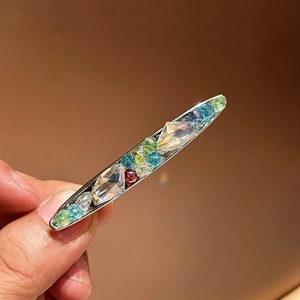 Détail d'une pince à cheveux argentée avec des cristaux colorés verts et bleus