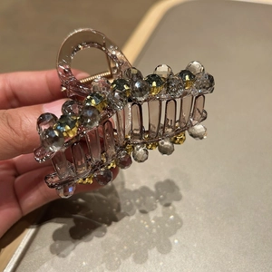 Detail of a brown resin hair claw clip with grey crystals and gold bead accents
