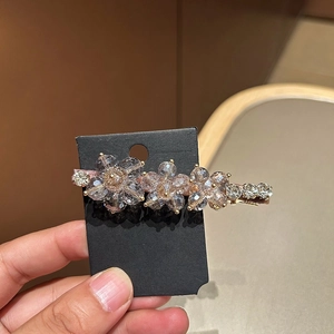 Blue crystal flower duckbill hair clip with golden bead accents on a black display card