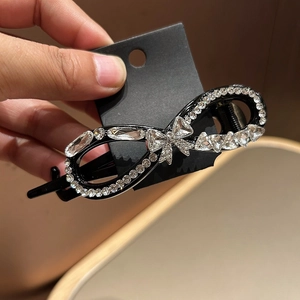 Detail of elegant black infinity hair clip with sparkling white rhinestones and a bow