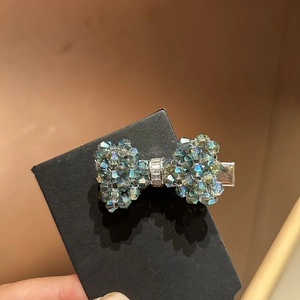 Detailed view of a crystal bow hair clip featuring shimmering teal beads and a silver band