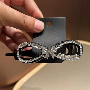 Detail shot of a bow-shaped hair clip with sparkling rhinestones on a black alloy base