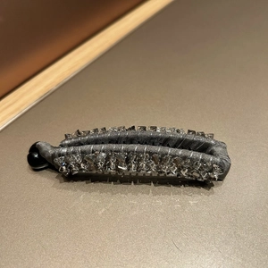 Macro detail of a grey fabric banana clip featuring sparkling crystal trim and a black buckle