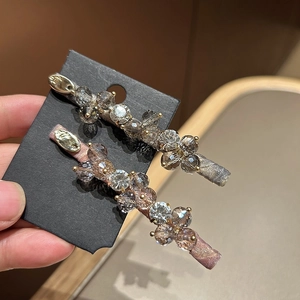Detail of two crystal flower hair clips in purple and grey on display card