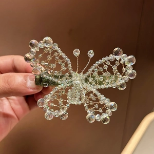 Detailed view of hand-woven crystal butterfly hair clip with gold wire and green satin base