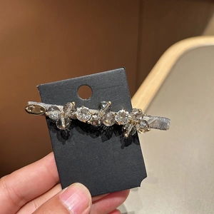 Elegant crystal hair clip with sparkling diamonds and gold logo on black card