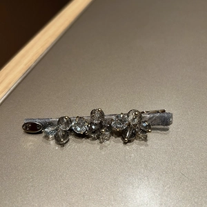 Detail view of gray crystal hairpin with satin fabric and silver metal logo tag