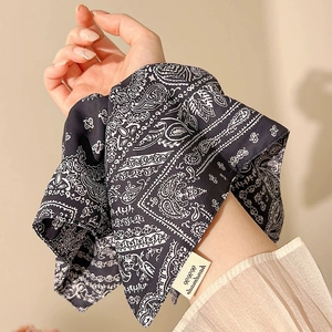 Detail of navy paisley square scarf tied on wrist with handmade label and silk texture