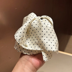 Close-up of cream satin scrunchie with black polka dots and an elegant gold oval charm