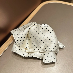 Detail of white silk satin hair claw with black polka dots and gold metallic logo