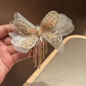 Détail d'une pince à cheveux papillon champagne avec paillettes et perles fines