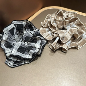 Detail of plaid fabric scrunchies in black and brown patterns on a beige surface