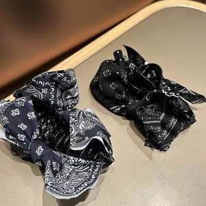 Detail view of two vintage paisley print bow hair claws on a textured grey surface