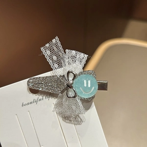 Dettaglio del fermaglio con fiocco in pizzo, strass e perla blu con smiley su carta regalo