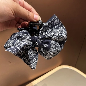 Handheld view of a vintage black paisley print fabric bow hair claw clip for women