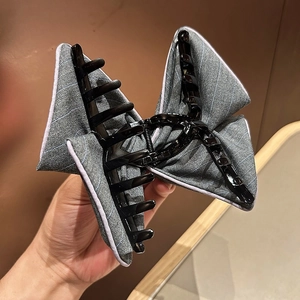 Detail shot of the grey striped fabric bow hair claw clip with black plastic teeth