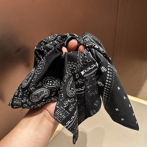 Detail of navy paisley scrunchie with long bow ribbon held by hand for hair styling