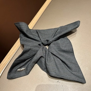 Detailed view of dark grey striped fabric hair tie with elegant metal brand tag