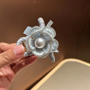 Detail of tweed camellia hair clip with shimmering rhinestones and a large center pearl