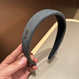 Detail of light grey striped fabric headband featuring a polished metal logo oval plate