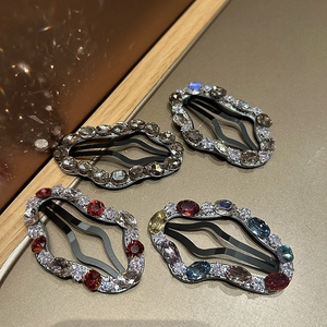 Detail view of four wave-shaped BB hair clips with colorful rhinestones on gold texture