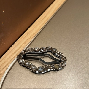 Close-up of sparkling rhinestone hair clip with dark grey crystals and black metal base