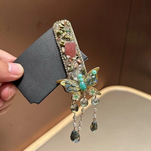 Vintage butterfly hair clip with green rhinestones and tassel charms in hand
