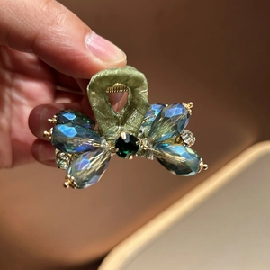 Detail of blue crystal bow hair claw clip with emerald green gem and gold accents