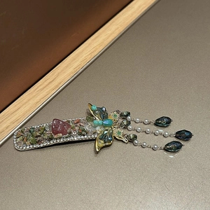 Detail of a green butterfly tassel hair clip with pink stones and blue crystals