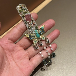 Detailed close-up of a vintage emerald butterfly hairpin with pearls and tassels